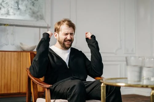 A frustrated man wearing a black tracksuit sitting on a wooden chair