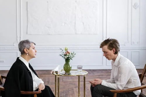 A patient dressed in a white shirt sitting in front of a psychiatrist