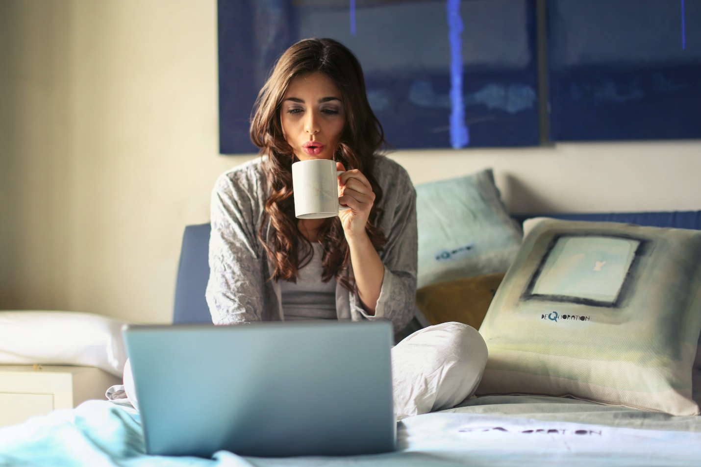 A woman using a laptop and having coffee on her bed