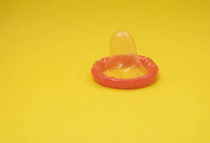 Unwrapped condom against yellow background.